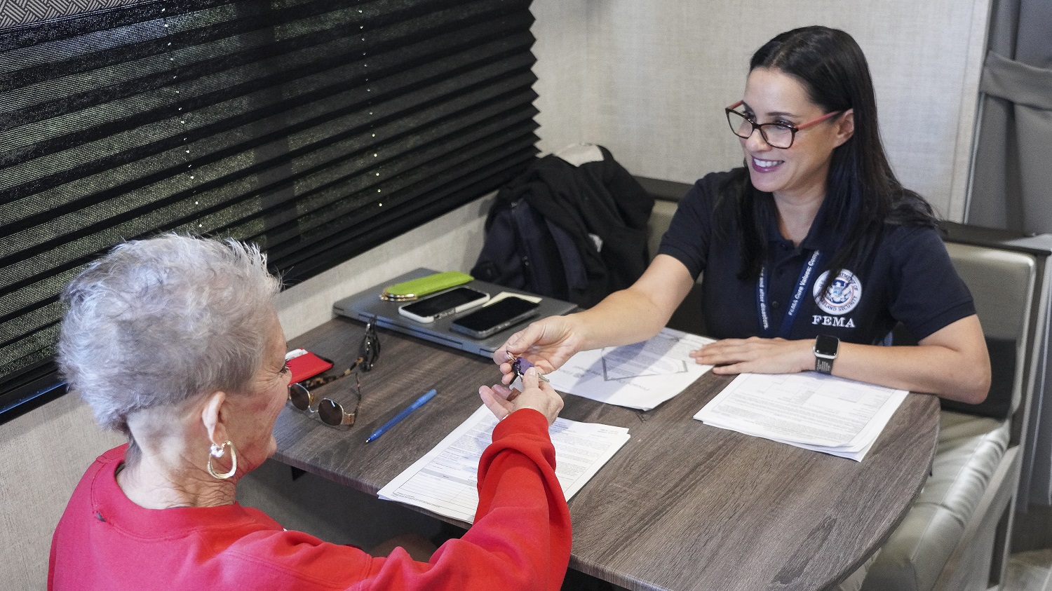 FEMA Local Hire employee behind a desk hands keys to trailer to an older woman.