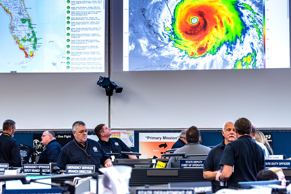 Men working in the hurricane monitoring office, with projection of large hurricane behind them.