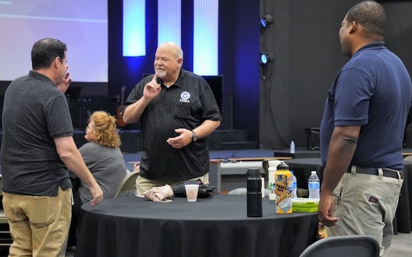 3 men standing around the table having a sign language conversation