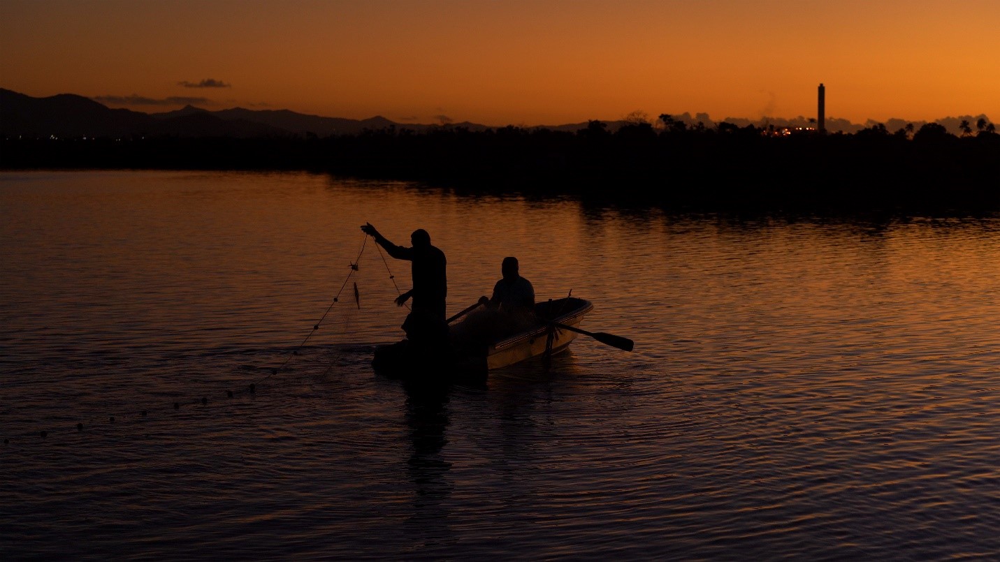 Two men fishing on a boat while the sun is setting. 