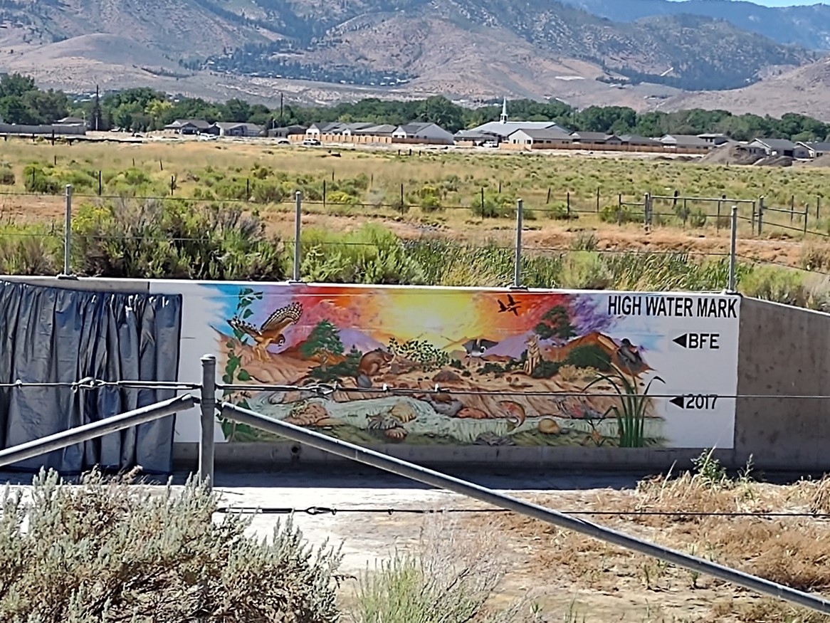 A photograph of a 10-foot by 30-foot mural with images of wildlife and vegetation. The right side of the mural shows two arrows that represent the base flood elevation and the current high water mark flood elevation.