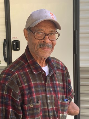 A man wearing a baseball cap, glasses, and a plaid shirt. He has a mustache.