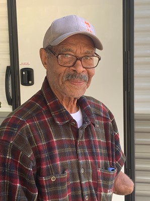 A man wearing a baseball cap, glasses, and a plaid shirt. He has a mustache. 