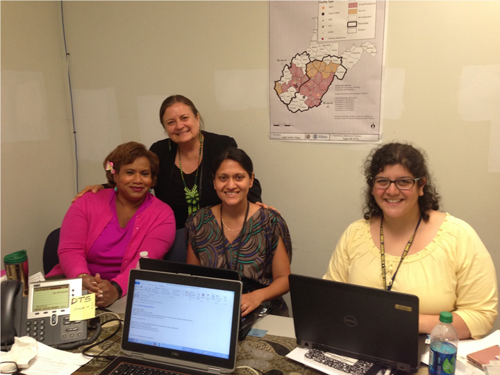 Four women smiling behind a desk with laptops