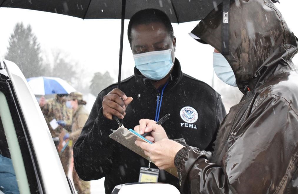 FEMA Worker holding a umbrella and another working signing a survivor up for vaccinations. 