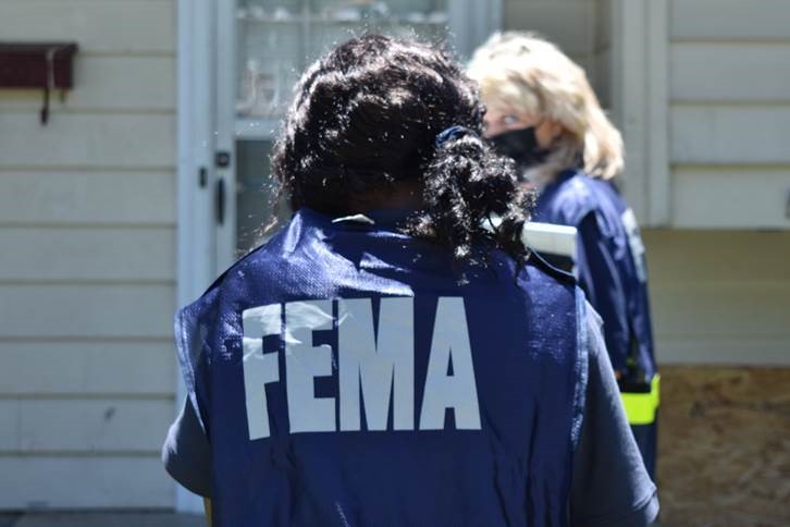 a female with her back turned from the camera with a jack with FEMA on the back and there is lady in front of her wearing the same jacket. 