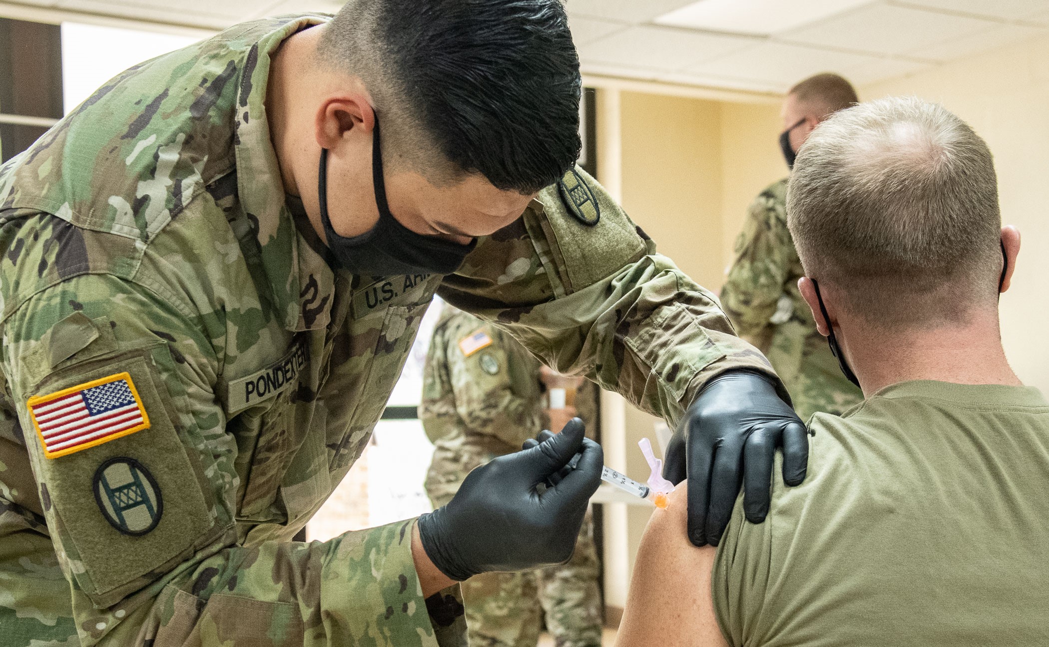 A male solider providing the vaccine shot to another male solider 