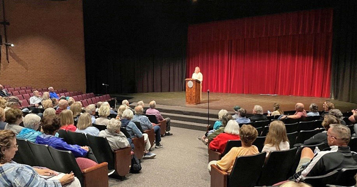 A woman behind a podium in an Auditorium.