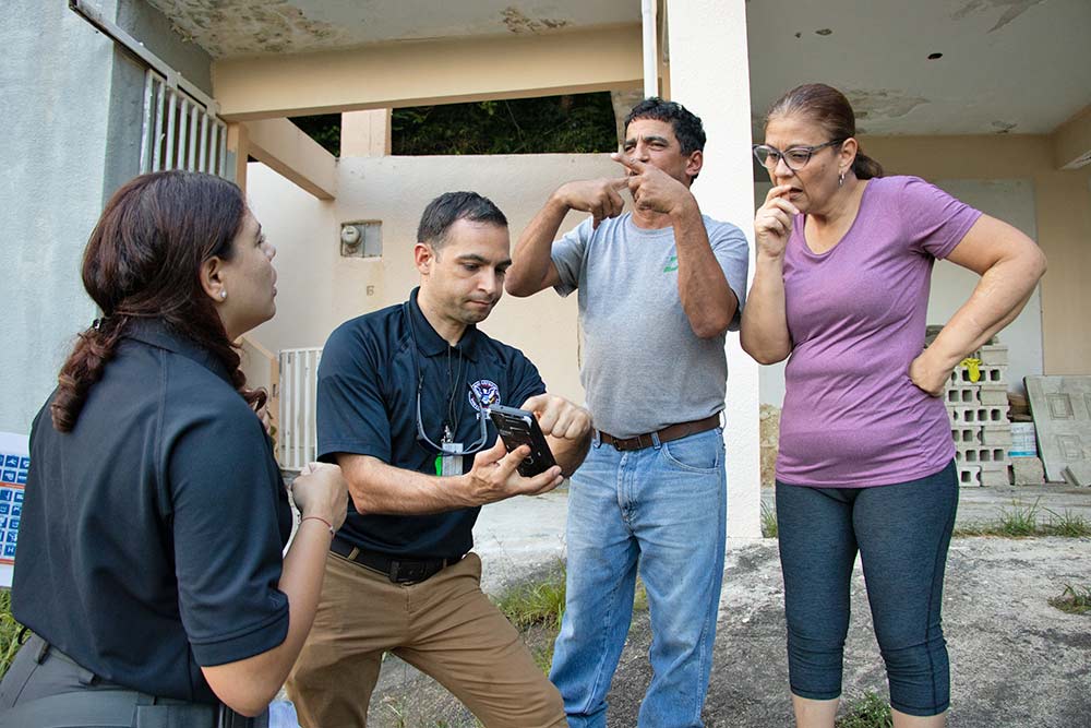 Four people in front of a damaged house.