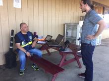 FEMA applicant services, helped more than 40 disaster survivors outside the Golden Eagle Market in Yuba County. Cesar is seated at a picnic table with computer equipment while Russell stands nearby. 