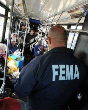 A FEMA employee stands on a bus of people 
