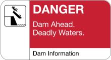 Sign reading: Danger Dam Ahead. Deadly Waters. Dam Information with a graphic of a stick figure falling out of a boat going over a dam. 