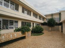 Two story beige building with outdoor terrace with brown tiles on floor.