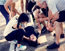 A group of people crouching around a woman laying passed out on the pavement