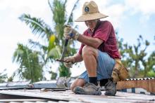 Man sitting on roof holding a hammer.