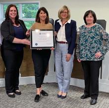 Four women standing together holding a plaque.
