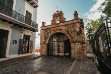 View of the entrance of the Capilla del Santo Cristo de la Salud. Entrance has a large brick wall with an iron gate.