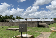 Front view of water treatment plant. In front there is grass followed by the cement structure with water.