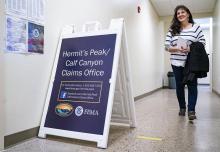 Woman walks by a sign announcing FEMA's Hermit's Peak/Calf Canyon Claims Office 