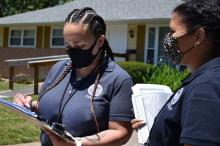 two females with blue FEMA polo shirts on and wearing face mask looking a papers on a clip board