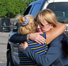Two women hug in front of vehicle.