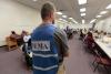 Man in a light blue vest with FEMA imprinted in the back faces the crowd of survivors waiting for help 