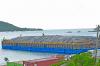  A barge with tarpaulin that is covering debris sits in the water with an island in the background. 